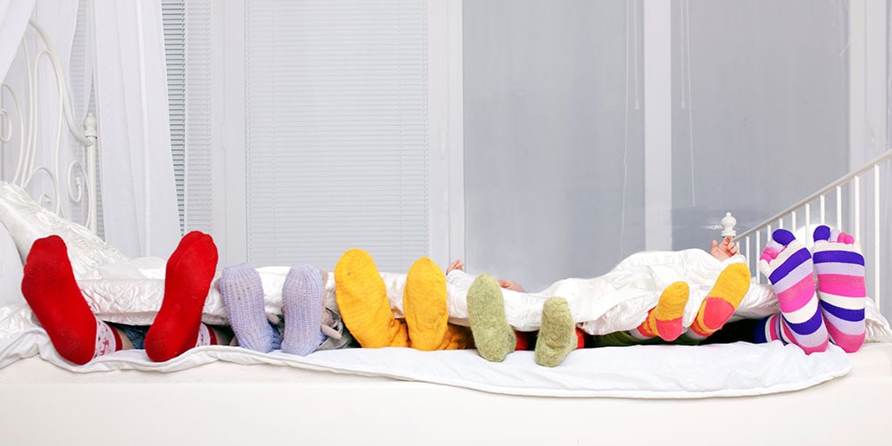 Row of feet in colorful socks lying in bed