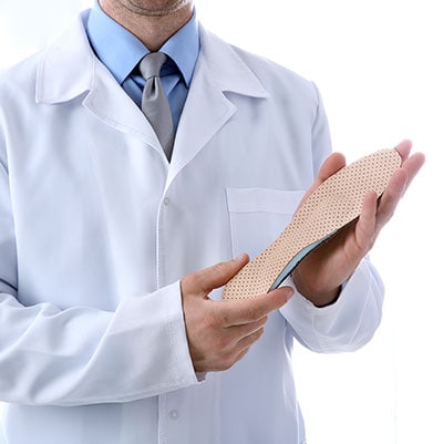 Doctor in white lab coat holding up orthotic shoe insert