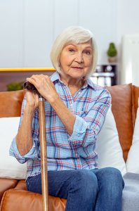 Older woman sitting on couch holding walking cane