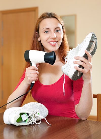Woman warming running shoes with hair dryer